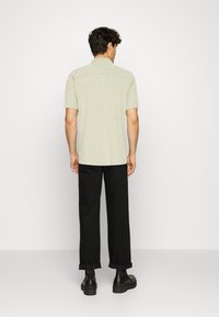 Hellgrünes kurzärmliges Hemd mit geradem Schnitt und Rückenpasse, kombiniert mit schwarzen, hochgekrempelten Hosen und klobigen schwarzen Stiefeln.