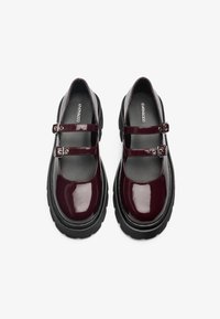 Bordeauxfarbene Lackleder-Mary-Jane-Schuhe mit schwarzen, klobigen Sohlen, die vorne zwei verstellbare Riemen und eine glatte Oberfläche aufweisen.
