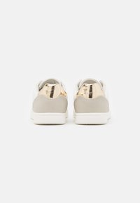 Vita sneakers med en mjuk läderöverdel, grå mockadetaljer vid hälen och en metallisk gyllene hälskydd. Platt, strukturerad gummisula.