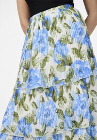 Jupe à volants florale en tissu léger et plissé. Elle présente des fleurs bleues et des feuilles vertes sur fond blanc. Taille élastique.
