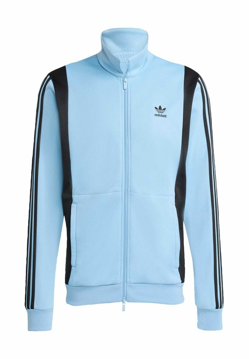 Veste zippée bleu clair en tissu texturé, avec des accents noirs et trois bandes noires le long de chaque manche. Comprend deux poches à l'avant.