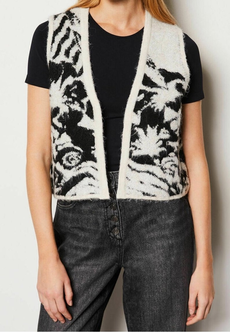 Femme portant un gilet duveteux à motif floral noir et blanc sur un haut noir à manches courtes avec un jean gris foncé taille haute.
