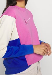 Color-blocked sweatshirt in pink, blue, and cream; features a small silver swoosh logo. Soft fabric with a relaxed fit and ribbed cuffs.