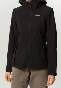 Giacca softshell nera con chiusura a zip, cappuccio regolabile, tasche laterali con zip e dettaglio logo discreto, caratterizzata da un design aderente e una finitura strutturata.