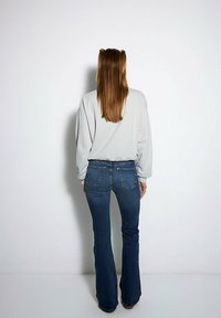 Szary, oversize'owy sweatshirt z ribbanym pasem, zestawiony z niebieskimi dżinsami w kształcie dzwonów. Dżinsy mają tylne kieszenie oraz subtelne detale zdobnicze.