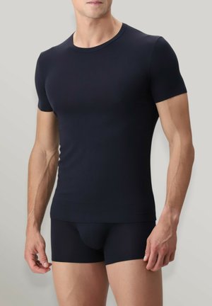 T-shirt attillato a maniche corte di colore blu navy, realizzato in tessuto liscio, con scollatura a girocollo e lati senza cuciture. Indossato con pantaloni coordinati.