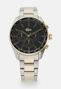 Montre chronographe ronde avec un cadran noir, accents dorés, bracelet en acier inoxydable argenté et échelle tachymétrique ; comprend trois sous-cadrans.