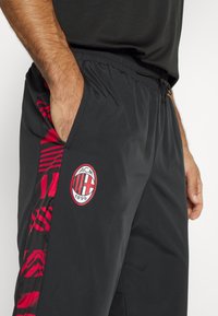 Svarta träningbyxor med ett rött och svart mönster på sidan, med en broderad logotyp. Lätta och elastiska midjeband med fickor.