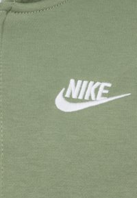 Πράσινο βαμβακερό ύφασμα με ριγέ υφή που διαθέτει λευκό κεντητό λογότυπο Nike. Το σχέδιο είναι απλό χωρίς επιπλέον σχέδια ή διακοσμητικά στοιχεία.