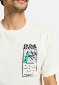 Cotton t-shirt, cream color, featuring a graphic print with a cactus and flower illustration. Accented with bold black text and geometric shapes.