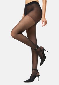 Medias negras transparentes con cinturilla reforzada, textura suave y apariencia opaca en las piernas, combinadas con zapatos de tacón altos negros.