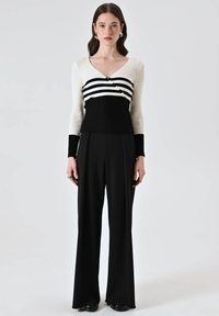 Top a righe nero e bianco con scollo a V e maniche lunghe, abbinato a pantaloni neri a gamba larga a vita alta. Texture lisce.