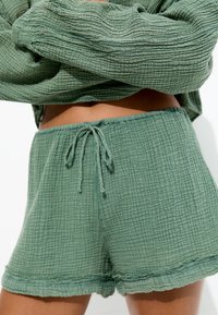 Shorts verts à cordon de serrage en tissu doux, portés avec un haut assorti à manches longues, dévoilant le ventre et affichant une coupe décontractée et confortable.