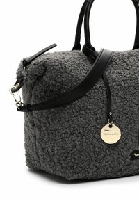 Hallikat tekstuuriga kangast käekott musta nahast käepidemete ja rihmaga; sellel on ümmargune metallist märk ja siledad mustad detailid.