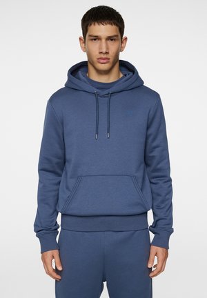 Blå hoodie med en frontal kengurulomme, snoretræk i hætten, ribbede manchetter og talje. Indeholder et lille logo på brystet.