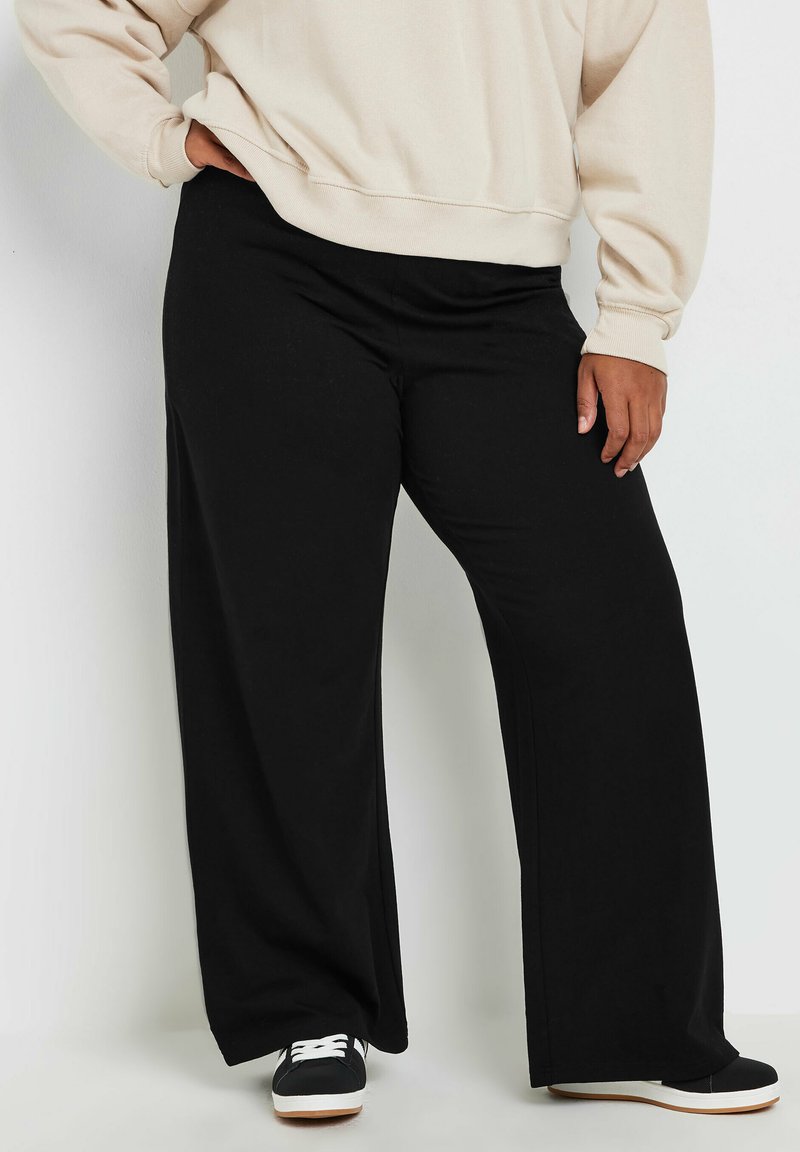 Pantalons larges noirs en tissu doux, avec une taille haute et une coupe décontractée, associés à des baskets noires et un sweat-shirt beige.