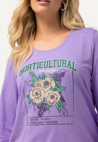 Camisa de manga larga morada con un gráfico floral de rosas y uvas. El texto dice "Sociedad HORTICULTURAL" en verde sobre el diseño.