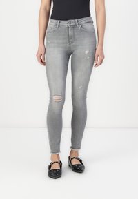 Jeans ajustados grises con detalles desgastados, que presentan desgarros en las rodillas y dobladillos deshilachados. Combinados con zapatos planos negros con remaches.