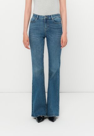 Flared denim jeans in medium wash with a slightly worn texture. Features five pockets and a zipper fly, paired with black heeled shoes.