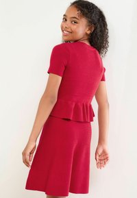 Rød strikket kjole med korte ærmer, peplum talje detalje og en flagrende nederdel. Glat overflade med et ribbet mønster gennem hele kjolen.