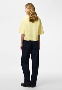 Gul ribbstickad tröja med korta ärmar, kombinerad med mörkblå vida jeans och svarta skor. Tröjan har en kort design.