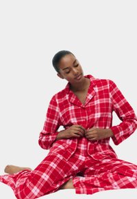 Rote karierte Flanell-Pyjamas mit langen Ärmeln und Knopfverschluss, ausgestattet mit einem klassischen Karomuster und weichem Material.