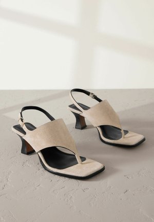 Beżowe zamszowe sandały z designem na palce, kwadratowym noskiem i blokowym obcasem. Posiadają czarny pasek w kostkę z metalowym detalem z klamrą.