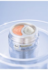 Crema per gli occhi doppia in un barattolo trasparente con un coperchio silver; un lato è pesche, l'altro è bianco. L'etichetta include il nome del marchio e i dettagli del prodotto.