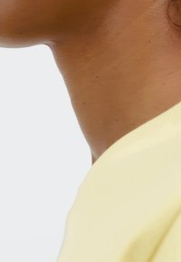 Žlutá bavlněná košile s kulatým výstřihem, přiléhavým střihem a žebrovaným lemem na límci. Hladká textura a minimální detaily.