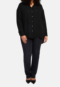 Svart skjorta med knappar och krage samt långa ärmar, med silverknappar. Kombinerad med mörka jeans och svarta högklackade skor.