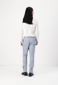 Pantaloni personalizați de culoare albastru deschis, cu o textură netedă, purtați cu o cămașă albă cu mânecă lungă, văzuți din spate pe un fundal simplu.