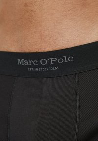 Svarta ribbade boxerkalsonger med en mjuk elastisk midjeband som har texten "Marc O'Polo EST. I STOCKHOLM" i grå bokstäver.