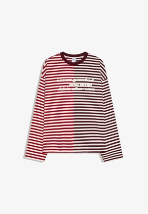 Košulja s dugim rukavima s vodoravnim crvenim i tamnosmeđim prugama, podijeljena na sredini, s bijelim tekstom preko prsa.