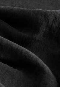 Tessuto nero con una superficie liscia e leggermente strutturata. Il materiale appare morbido e si drappeggia con grazia, mostrando sottili variazioni di tonalità.