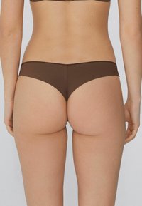 Brązowe majtki bikini z gładkiego, elastycznego materiału. Niski krój, minimalne pokrycie z zaokrąglonymi krawędziami i subtelnymi detalami ściegów.