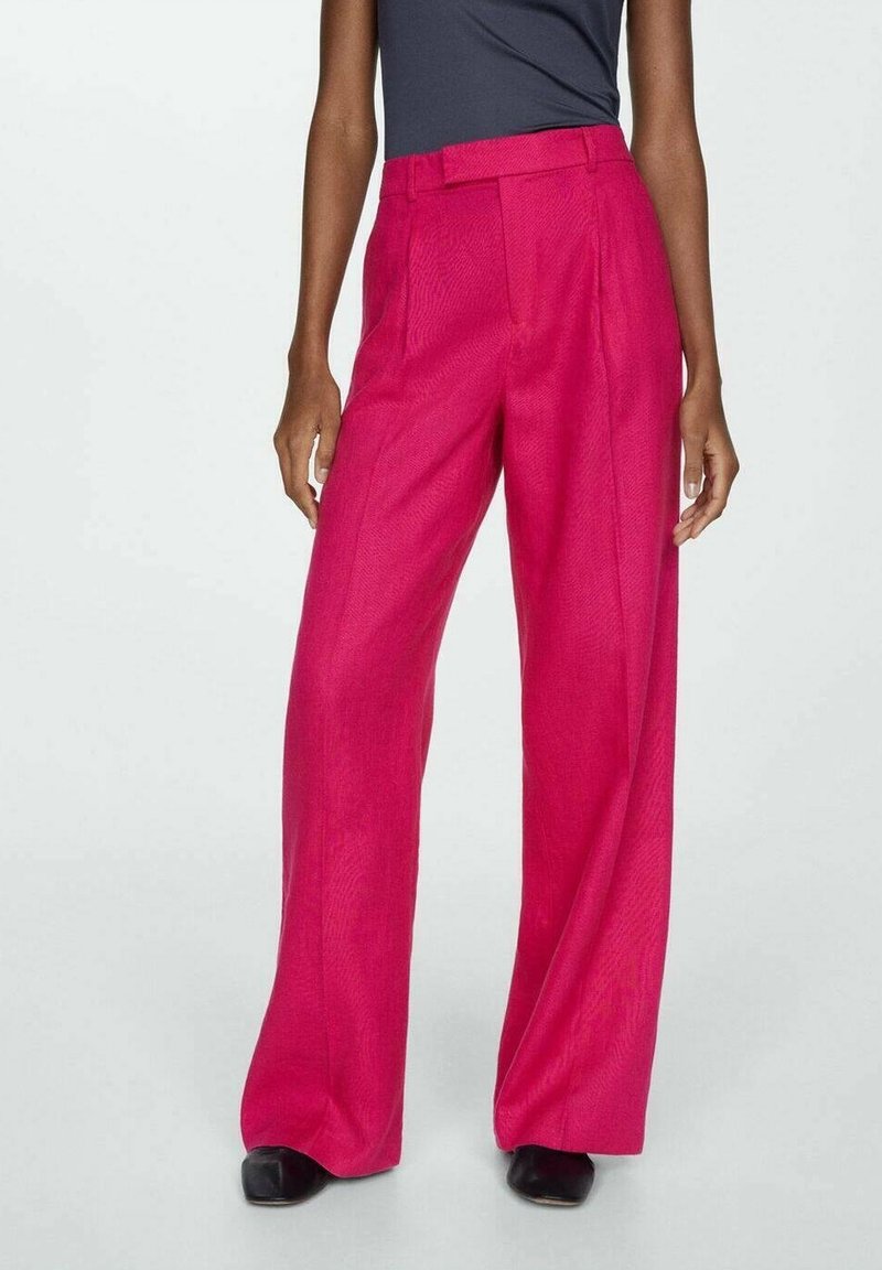 Pantalons évasés de couleur rose vif, confectionnés dans un tissu texturé. Ils présentent une taille haute avec des plis et des poches latérales. Des chaussures noires complètent le look.