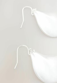 Hvide bladformede øreringe med sølvhooks, glat tekstur og minimalistisk design, der fremhæver lette og elegante træk.