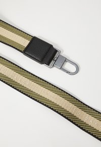 Textured black leather attachment with a patterned strap in olive green and cream, featuring "TED BAKER" branding in a repeating design.