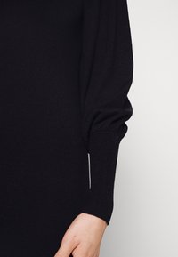 Maglione nero lavorato a maglia con texture a coste, maniche lunghe a sbuffo e polsini aderenti. Tessuto morbido con una leggera lucentezza.