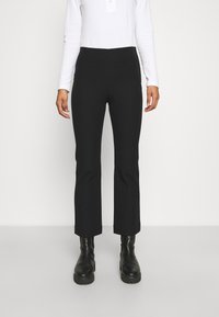 Černé kalhoty na míru s přiléhavým pasem, rovnými nohavicemi a zkrácenou délkou, doplněné černými robustními botami a bílým topem s dlouhým rukávem.