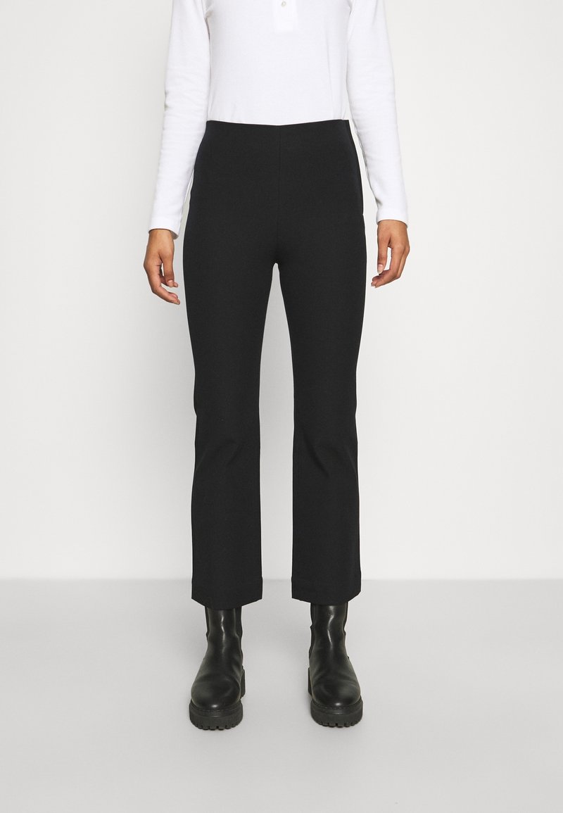 Černé kalhoty na míru s přiléhavým pasem, rovnými nohavicemi a zkrácenou délkou, doplněné černými robustními botami a bílým topem s dlouhým rukávem.