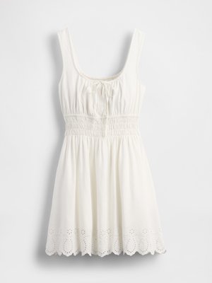 Bijela haljina bez rukava s kvadratnim izrezom, nabranim strukom, detaljem vezanja na prsima i rubom s valovitim uzorkom od čipke.