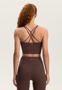 Barna crop top keresztezett pántokkal, texturált anyagból és hátul logóval, hozzá illő, magas derekú leggingsszel párosítva.