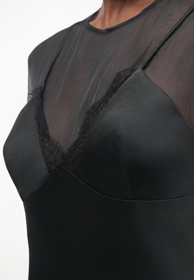 Μαύρο φόρεμα με διάφανη επάνω πανέλα, δαντελένια λεπτομέρεια κατά μήκος του λαιμού, και μια ομαλή, στενή σιλουέτα.