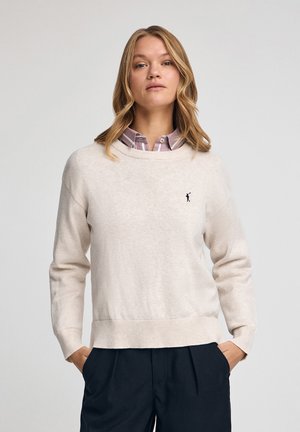 Helle beige Strickjacke aus weichem Stoff, mit langen Ärmeln, Rundhalsausschnitt, gerippten Bündchen und einem kleinen Logoakzent auf der Brust.