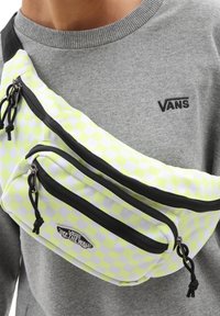 Sac banane à carreaux jaunes néon et blancs avec deux compartiments zippés et des accents noirs, porté sur un sweat gris.