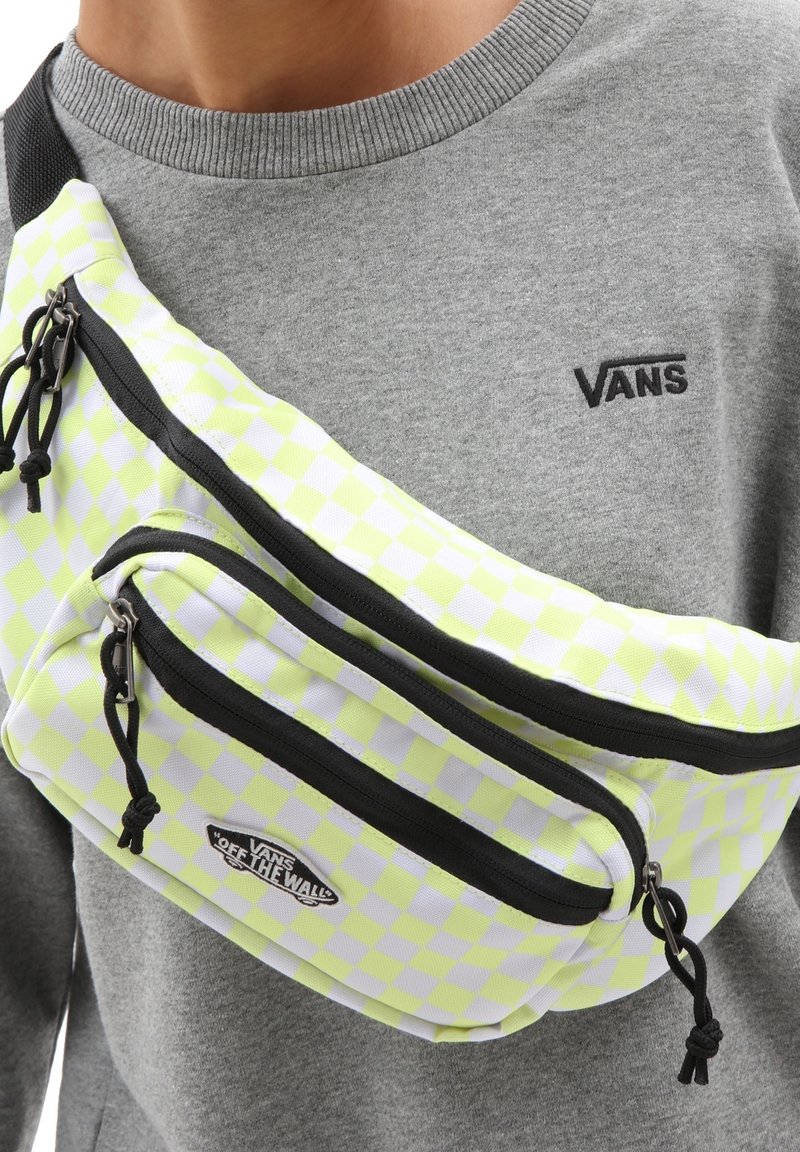 Sac banane à carreaux jaunes néon et blancs avec deux compartiments zippés et des accents noirs, porté sur un sweat gris.