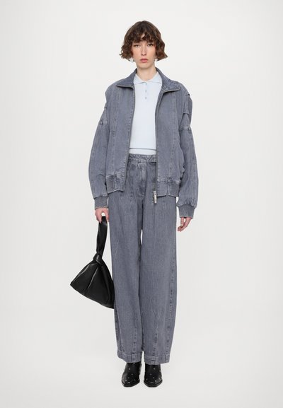 Jachetă din denim și pantaloni largi de culoare gri deschis, asortați cu un polo de culoare albastru deschis. Geantă neagră și cizme ankle cu ținte, din material texturat.