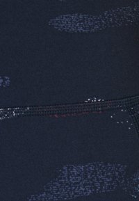 Tissu foncé avec des coutures encore plus foncées, présentant des motifs abstraits épars en violet clair et blanc.