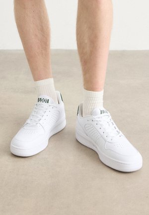 Zapatillas deportivas blancas con acentos perforados, cordones y suelas de goma gruesas. Combinadas con calcetines acanalados de color crema claro para crear contraste.